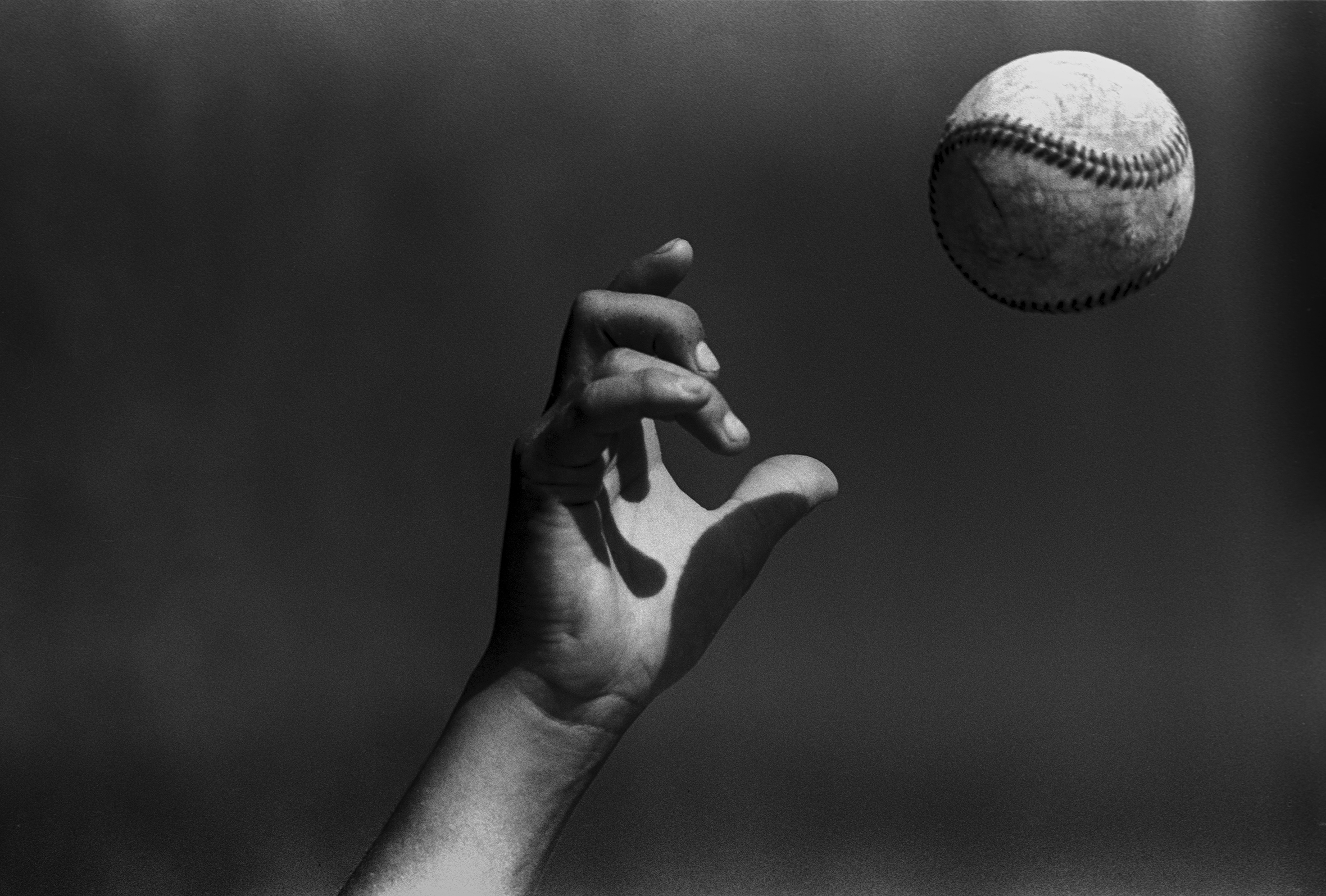 Close-up of a hand in the air and a just-released baseball. The fingers are positioned to have just thrown a curveball.