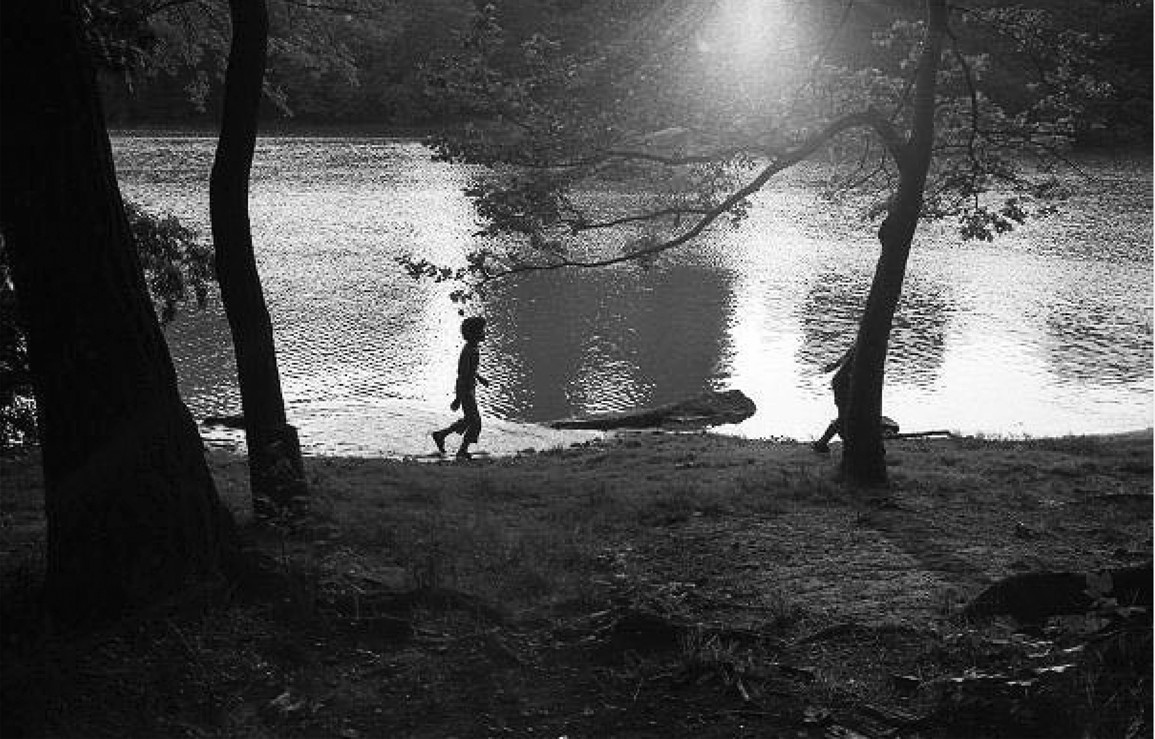 The silhouettes of two children as they walk along a lakeshore.