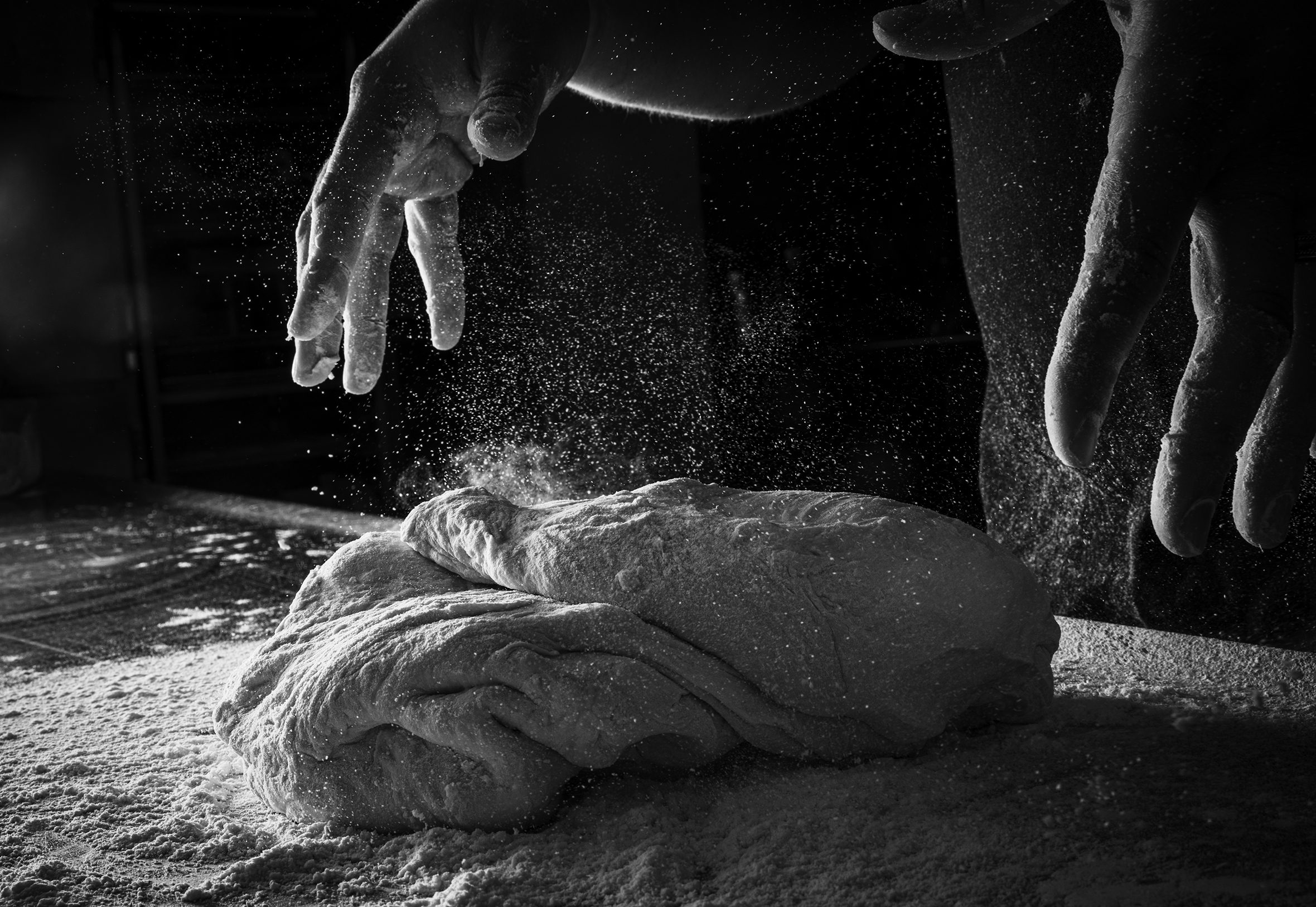 Close-up of hands throwing dough onto a floured table.