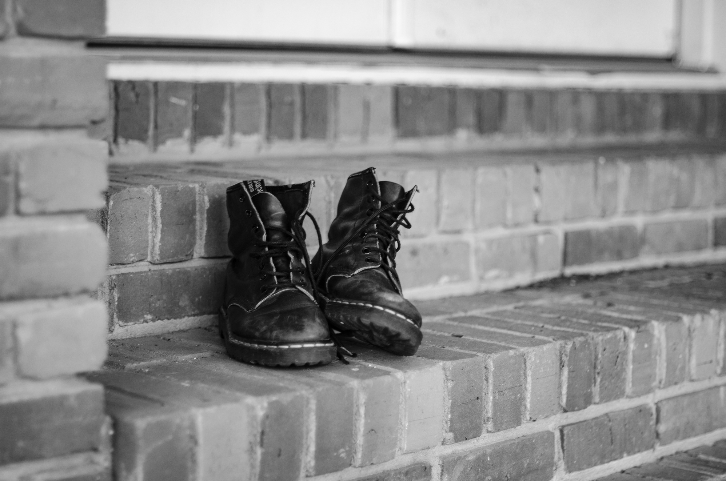 A close-up of black boots upon a brick step outside a door.