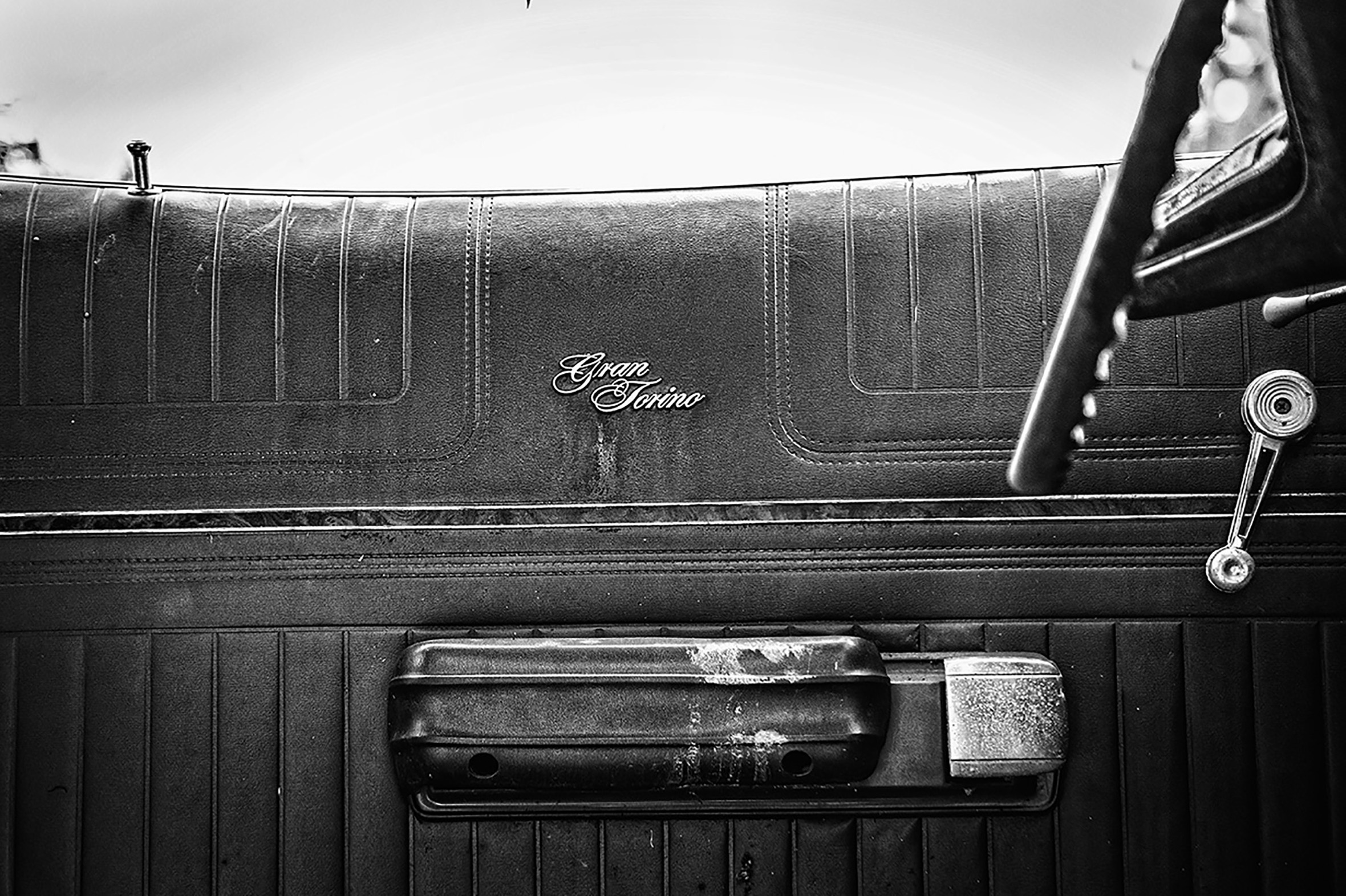 A close-up of the inside door of a Gran Torino. The steering wheel is just visible. The latch of the door is slightly worn.