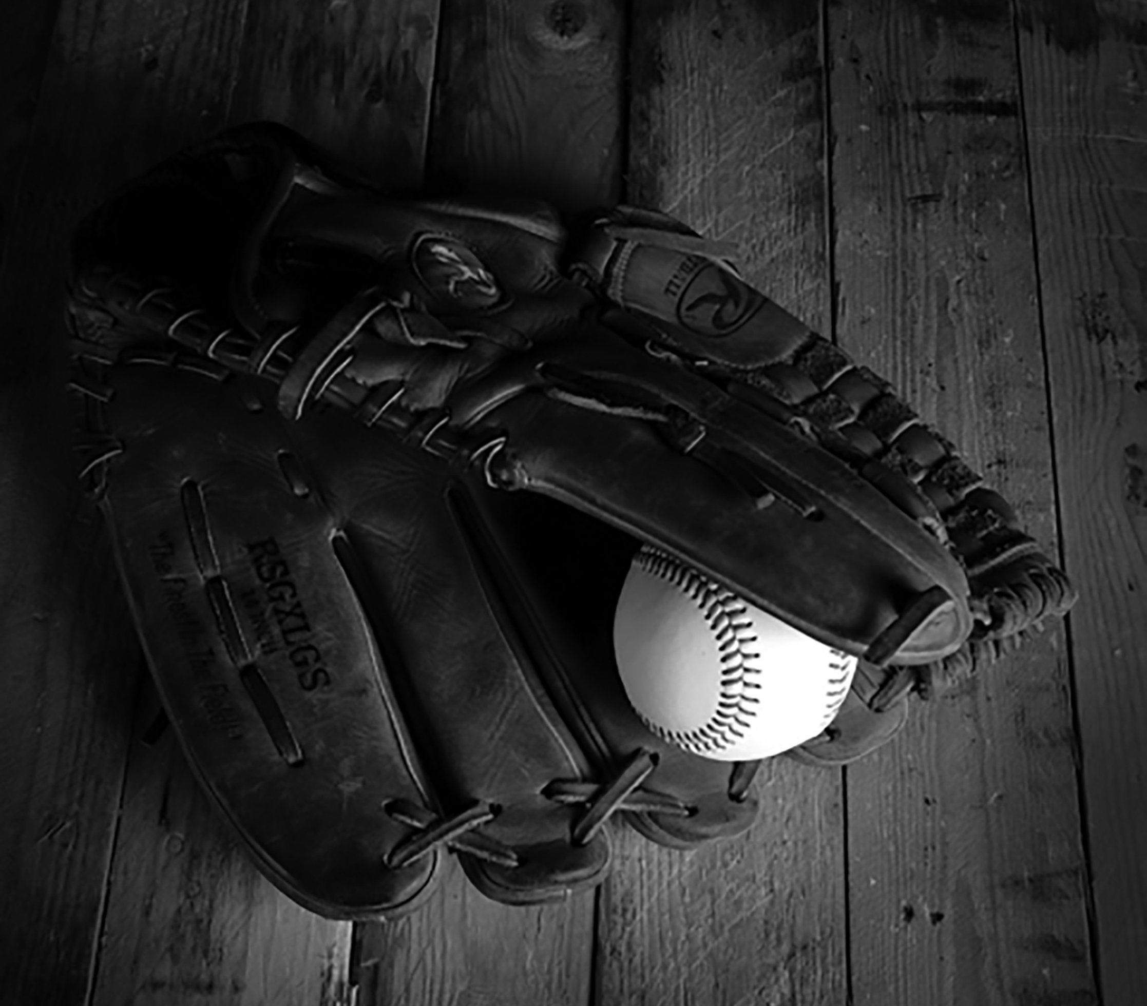 A close-up of a baseball glove on a wooden floor. A baseball is seen peeking inside the glove.