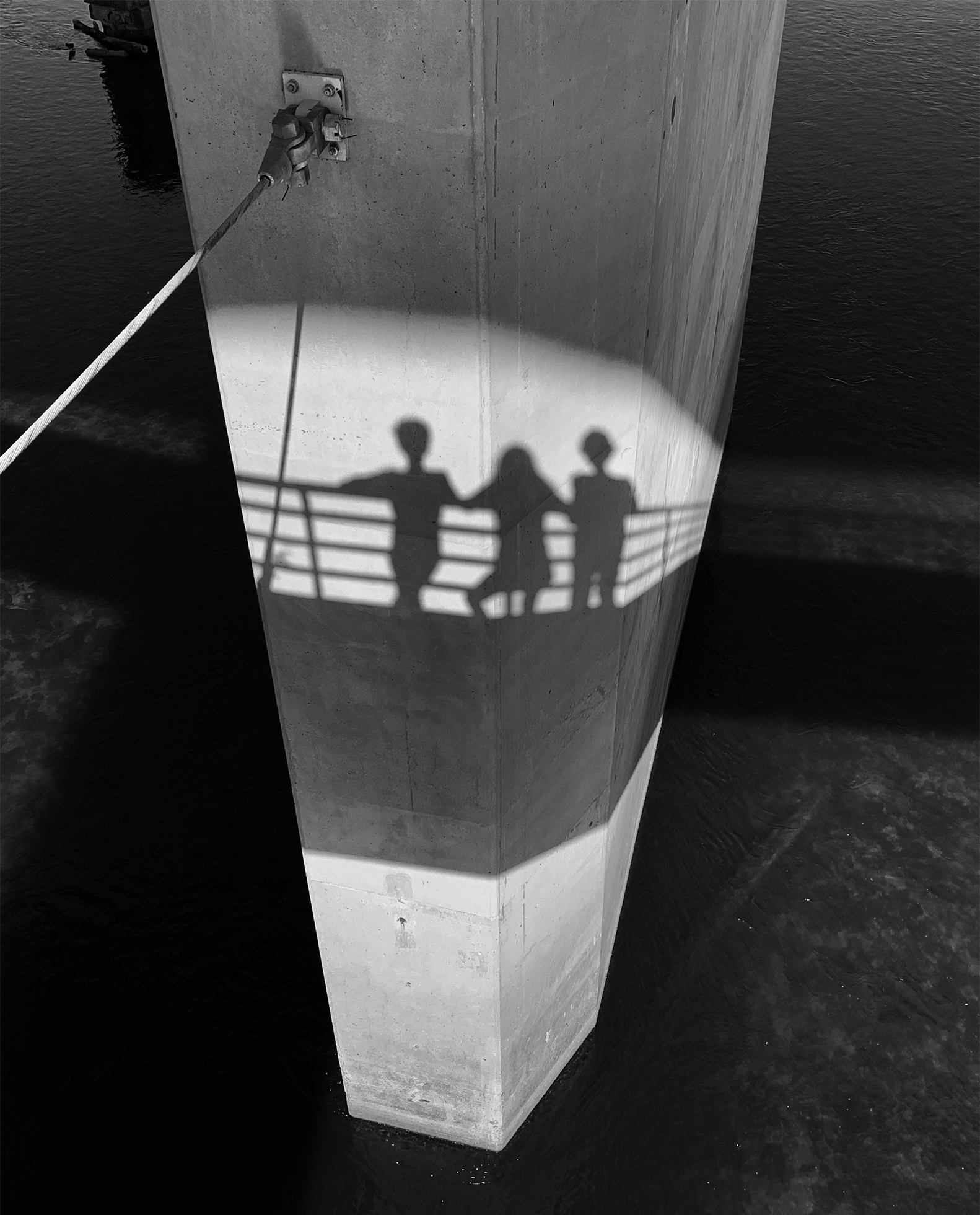 The reflection on a wharf pylon of three children on a gangway looking out at the water.