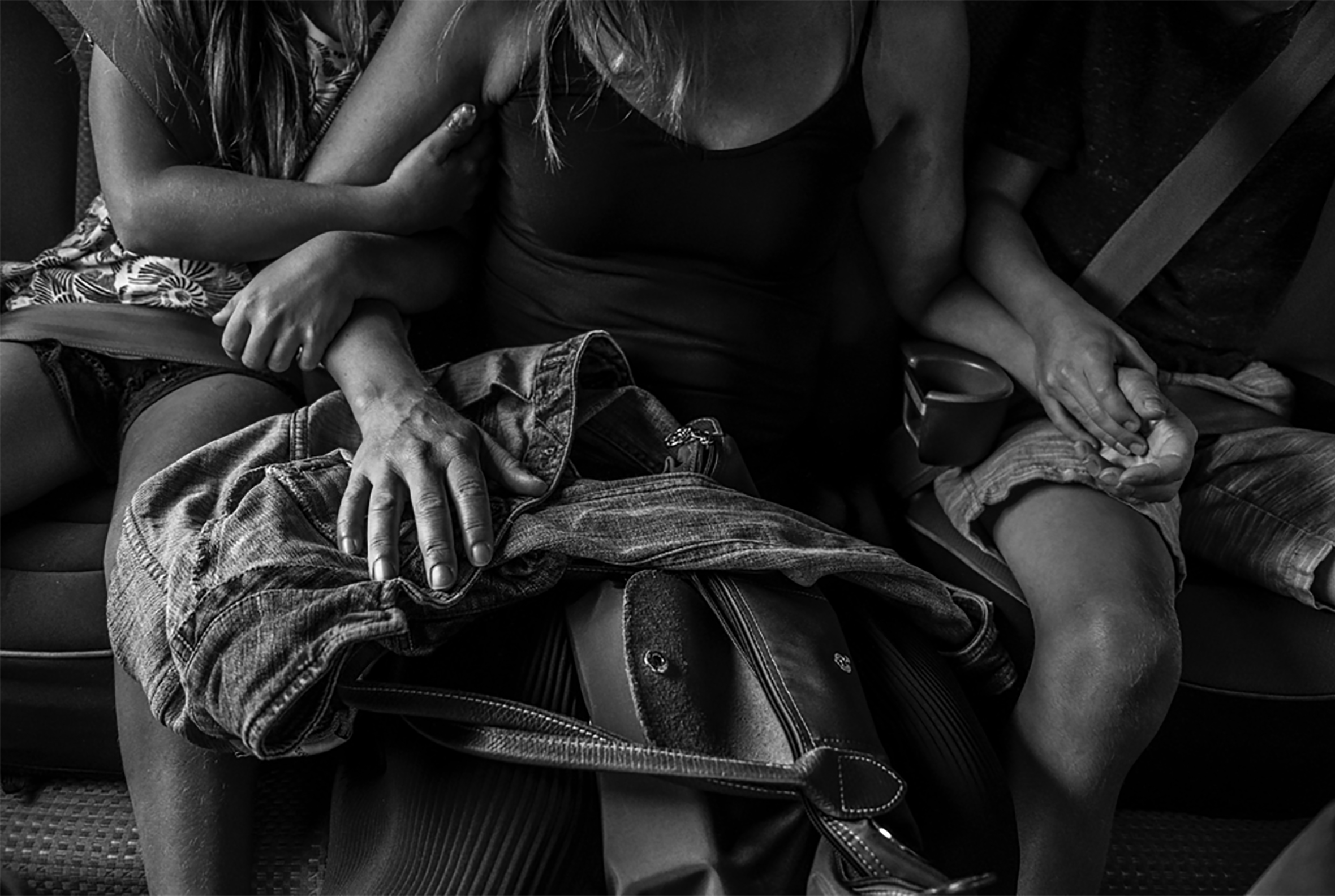 Two children sit on either side of their mother each holding her hand in the back seat of a truck.