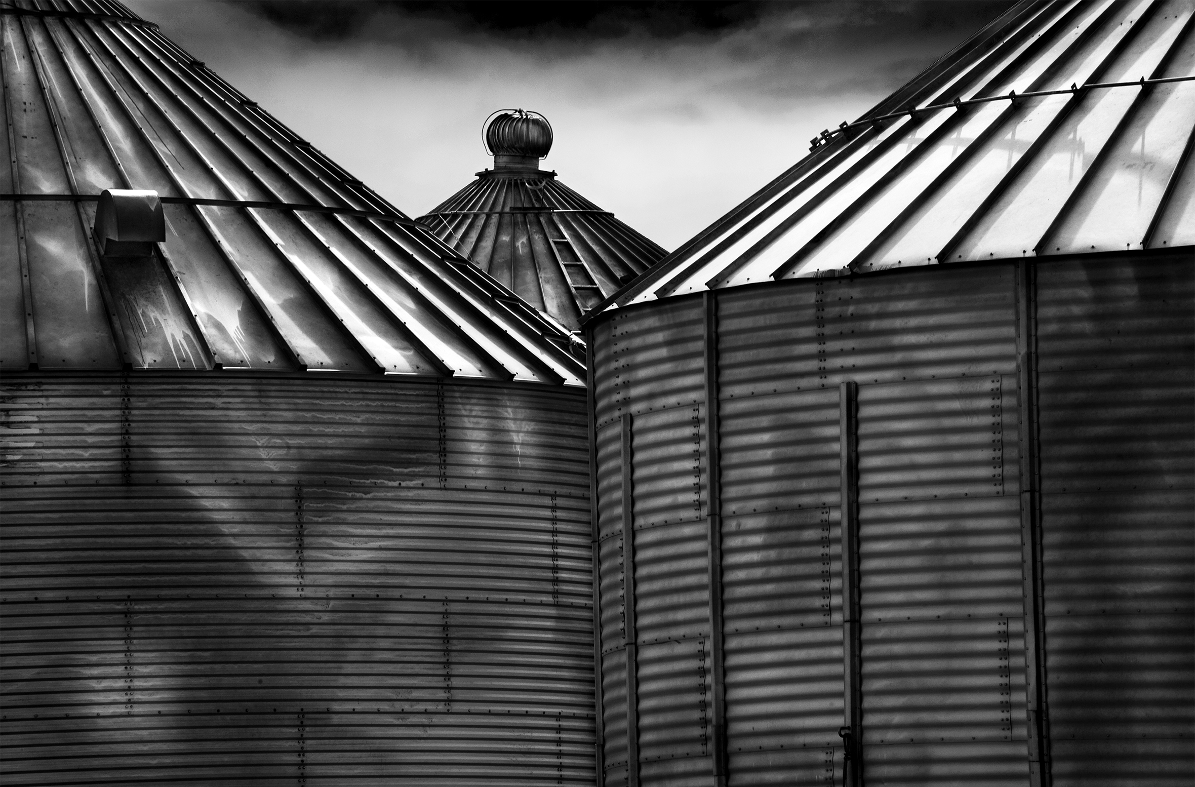 Close-up of the top portions of three grain silos, two overlapping in front and the third peeking out from behind and between them.