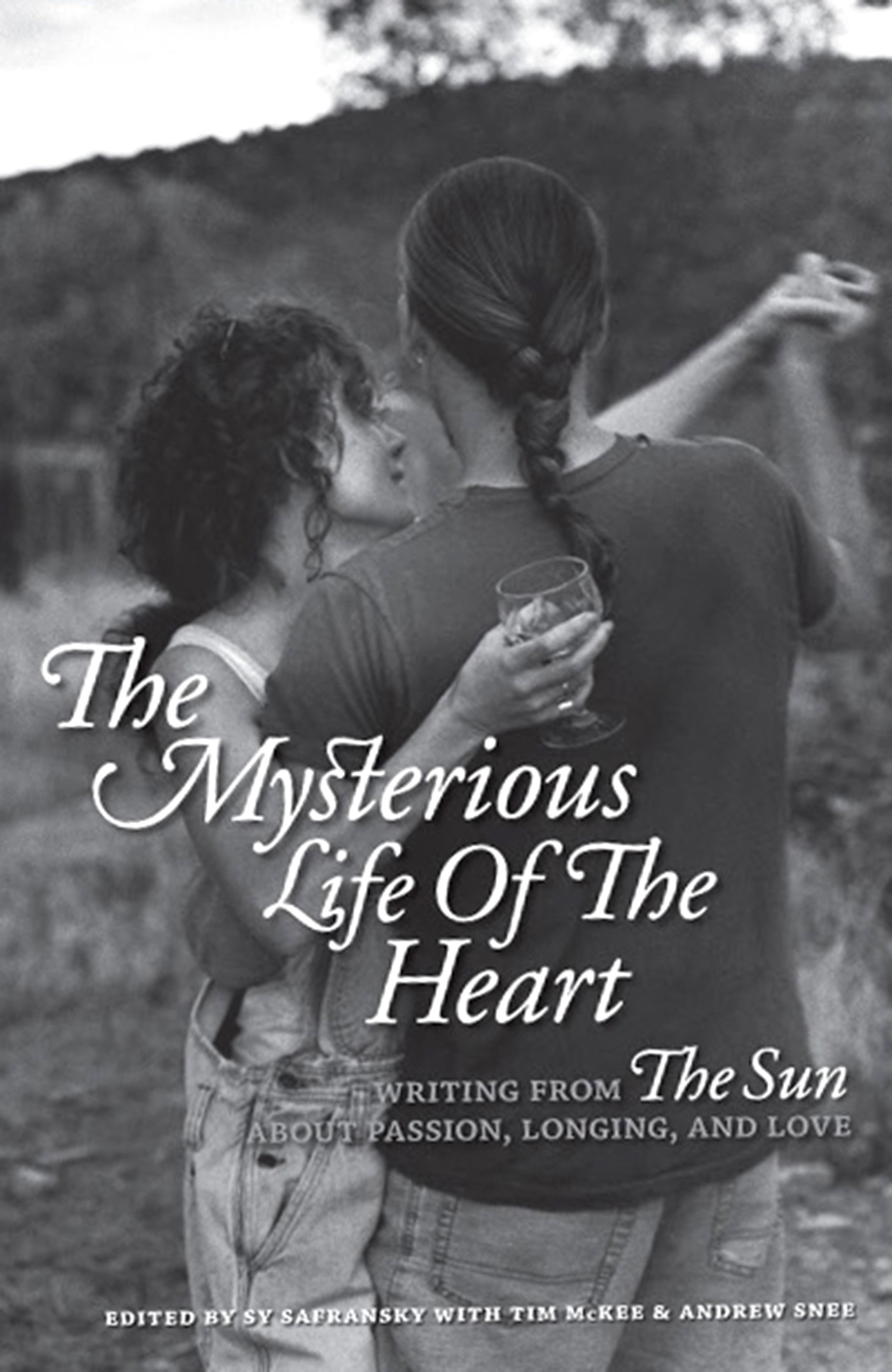 Book cover of “The Mysterious Life of the Heart.” A casually dressed couple dance together outdoors, wineglass in hand.