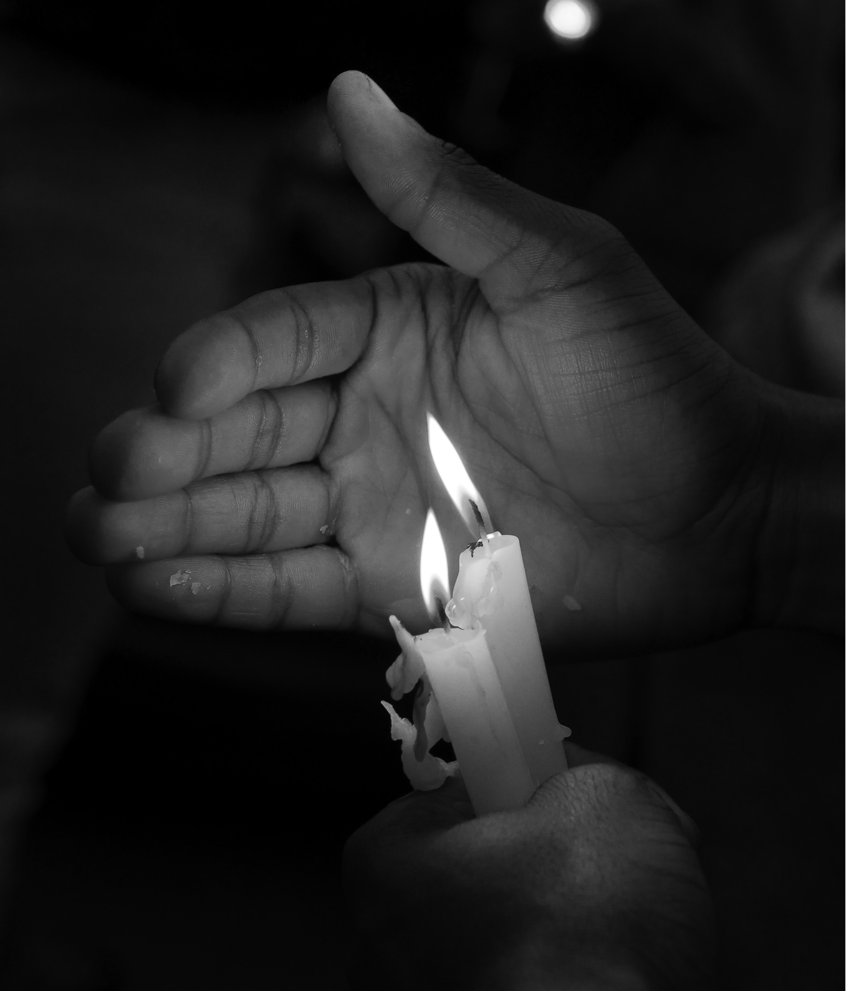 Close-up of two burning candles held in a person’s left hand while their right hand shields the flames.