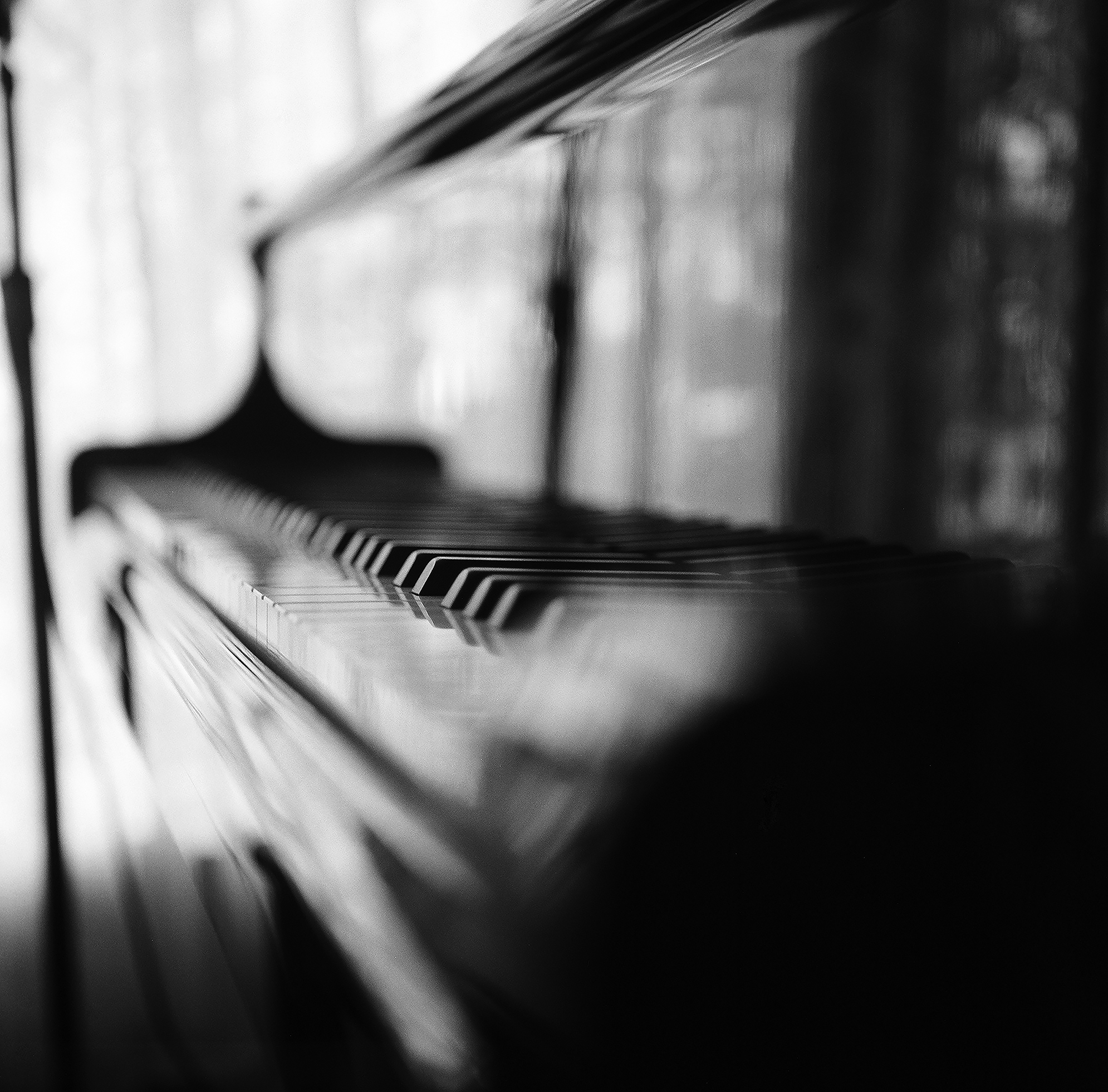 Blurry image of the keys of a shiny piano in front of a window.