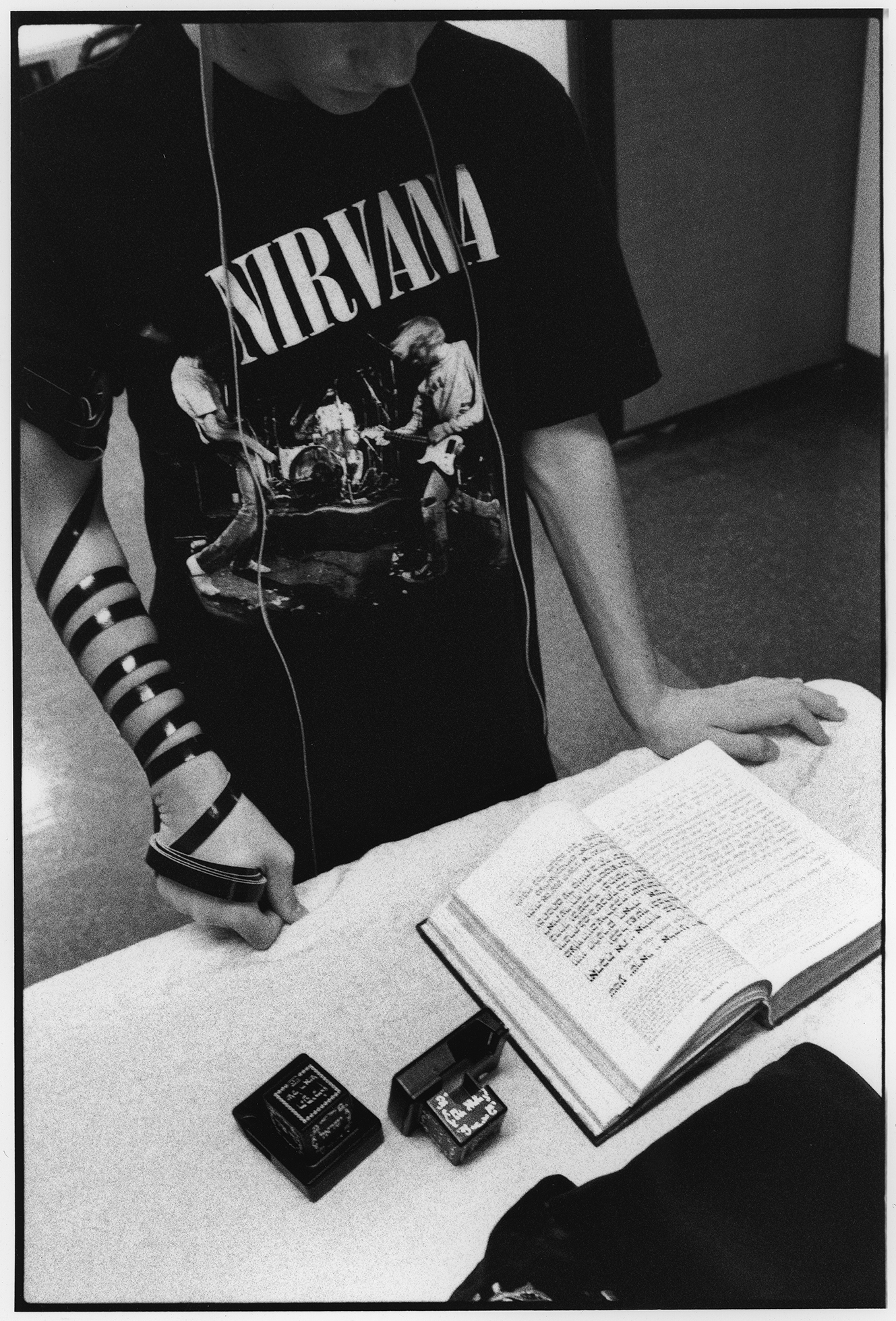 A young man in a Nirvana T-shirt with tefillin bound to his right arm is standing looking down at a book on a table and saying prayers at the Chabad of the Inland Empire synagogue in 2015.