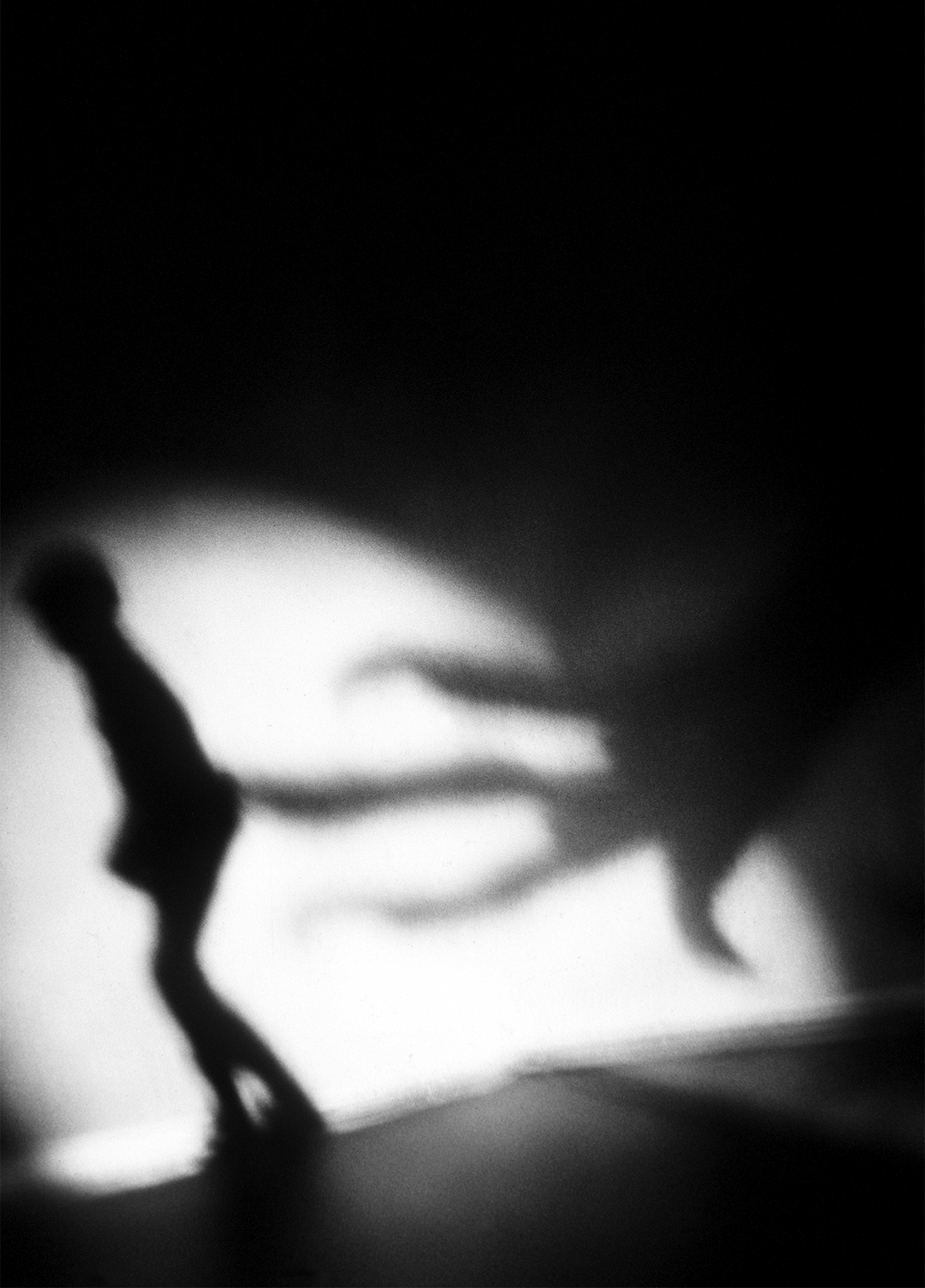 Dark, blurry image of the shadow of a small child in a spotlight on the wall with something reaching toward them.