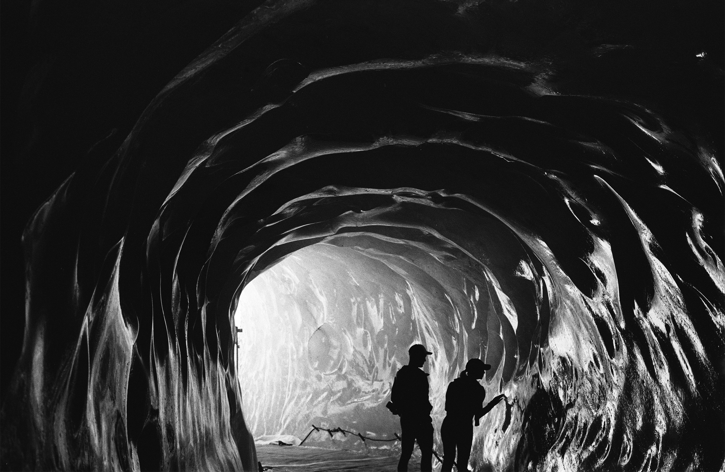 A man and a woman explore an ice cave in the Mer de Glace glacier, Mont Blanc, France. She is touching the side of the cave as he looks on.