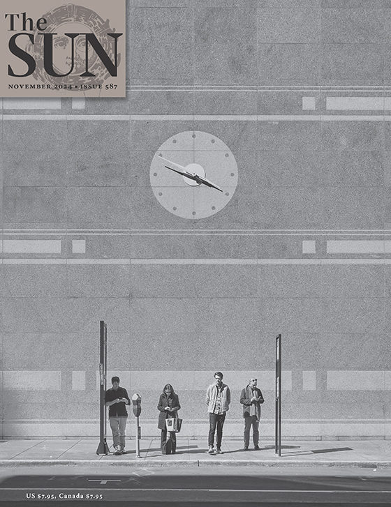 November 2024 cover of The Sun. Four people wait for a bus on Pine Street in San Francisco. Two men and a woman stand and look down at their phones and one man stands with his hands behind his back. The clock on the building behind them reads 3:50.