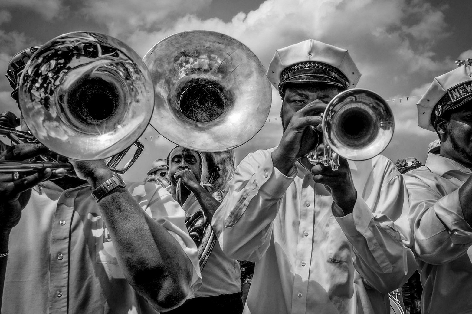 Several band members in a horn section perform during Mardi Gras in New Orleans. The band members are wearing white button-down shirts and white hats.