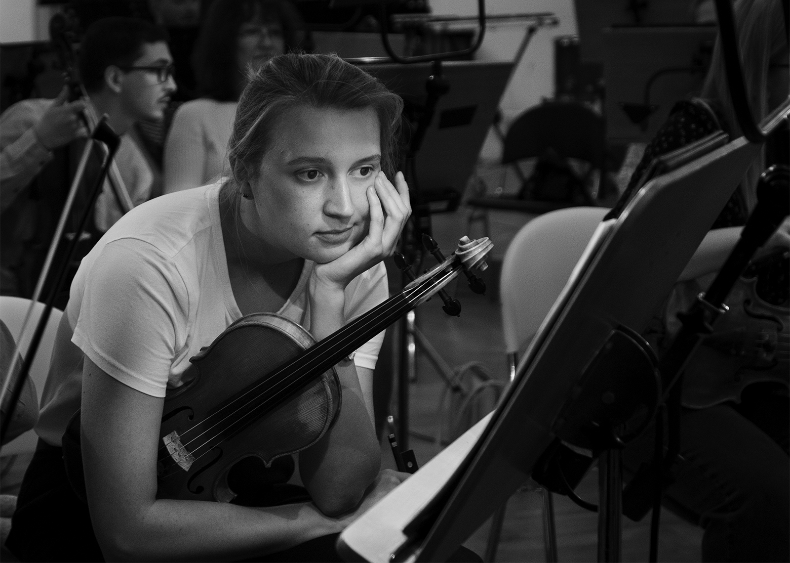 A violinist sits and stares at the sheet music on a stand in front of them during a pause in rehearsal.