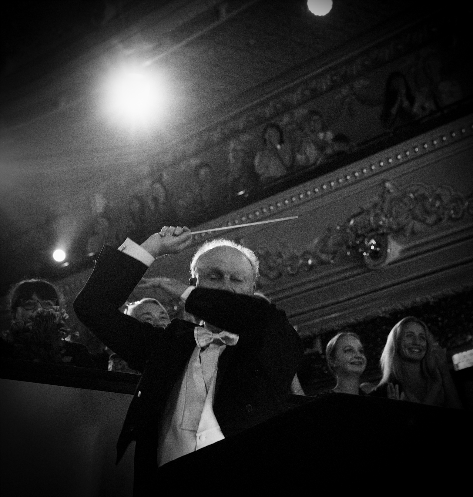 Orchestra conductor during a performance with the baton raised behind his head.