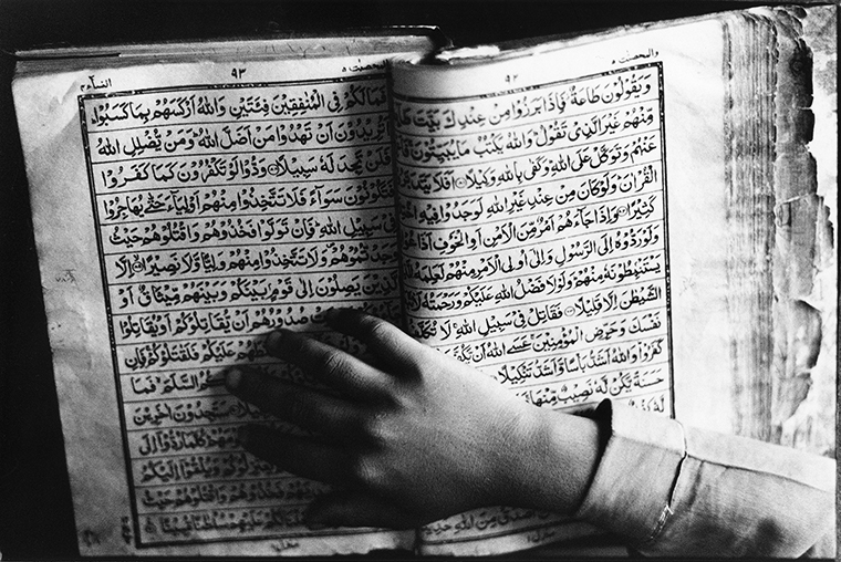 Close-up of the Quran with a hand atop holding the book open.