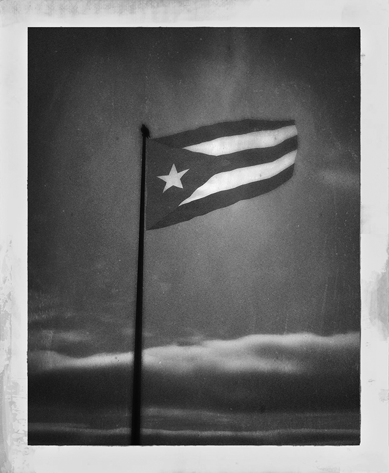 The top portion of a flagpole flying the flag of Puerto Rico on a partly cloudy day.