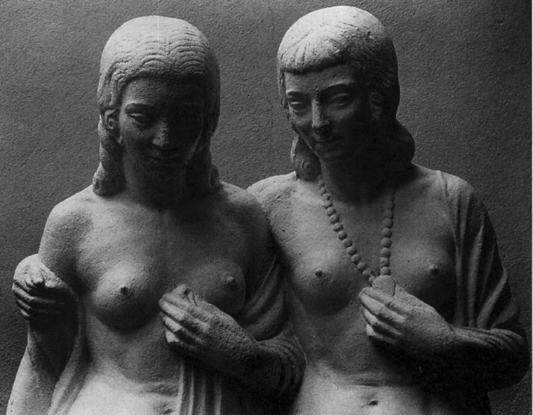 Statue of two nude women standing side by side facing the camera. The woman on the right has her arm around the woman on the left. Both are gazing downward and smiling slightly. Each has a shawl draped in the front around their upper arms.