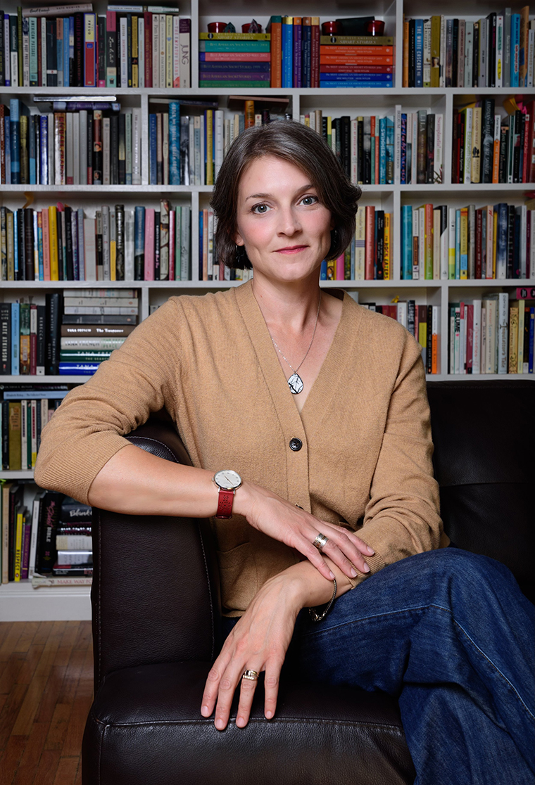 Photograph of Kirsten Sundberg Lunstrum seated facing the camera in front of a large bookcase.