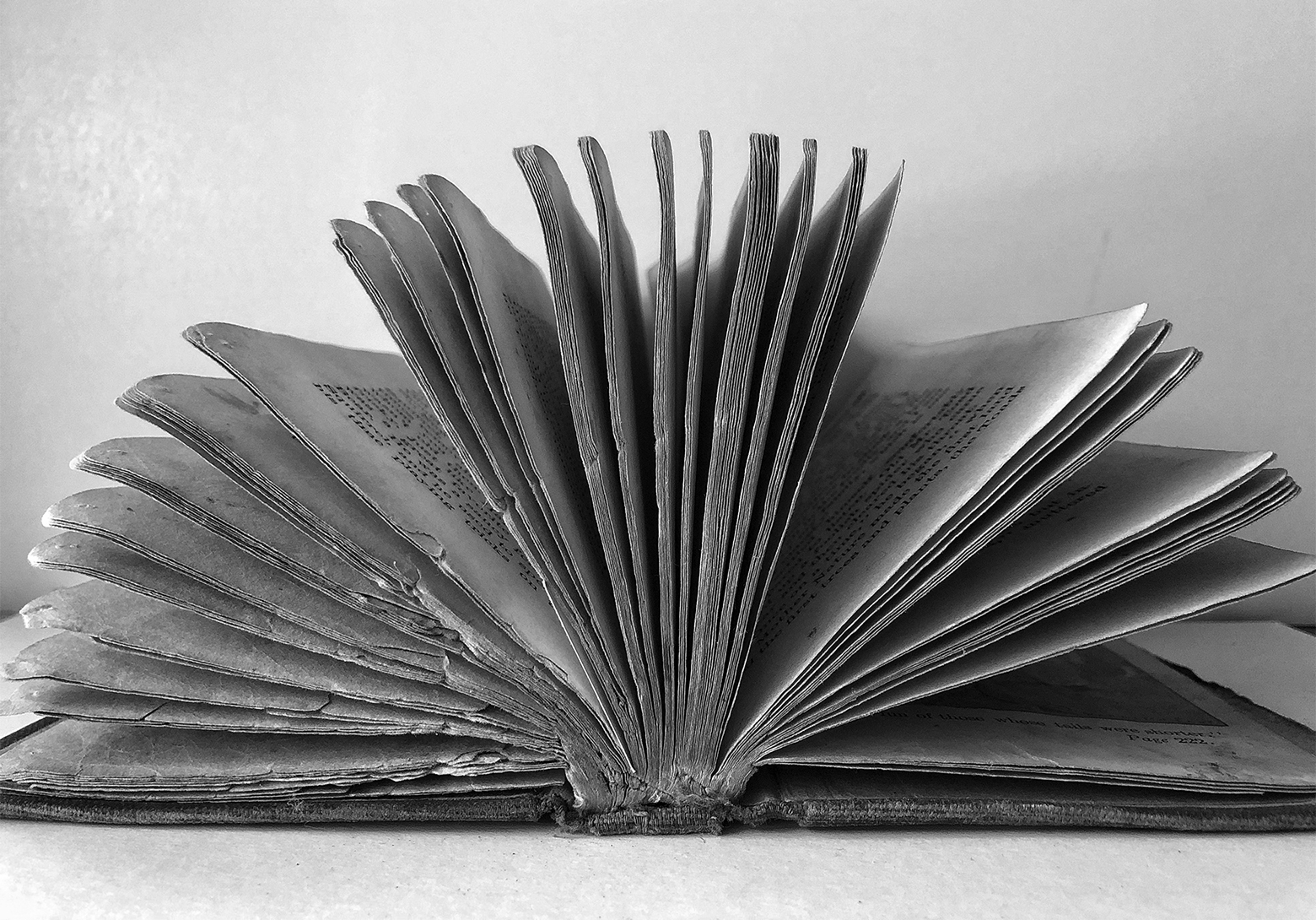 Hardcover book with worn covers, spine, and pages open flat on a level surface. The pages are spread open vertically in a half-moon shape.