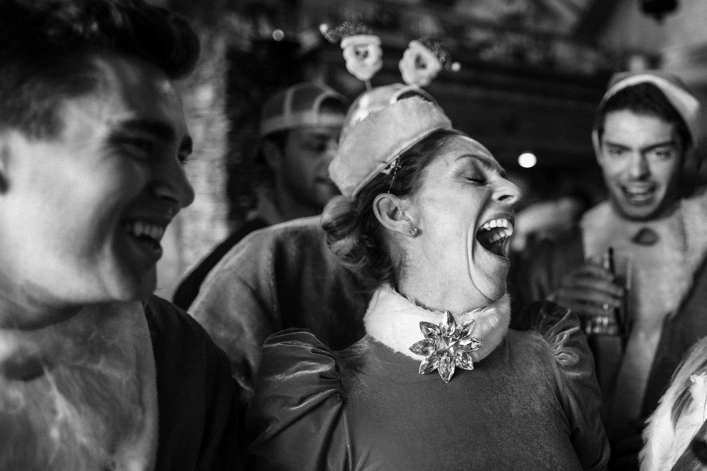 A holiday celebration in a downtown Boston bar where people dressed as Santa embrace the season and share a laugh.