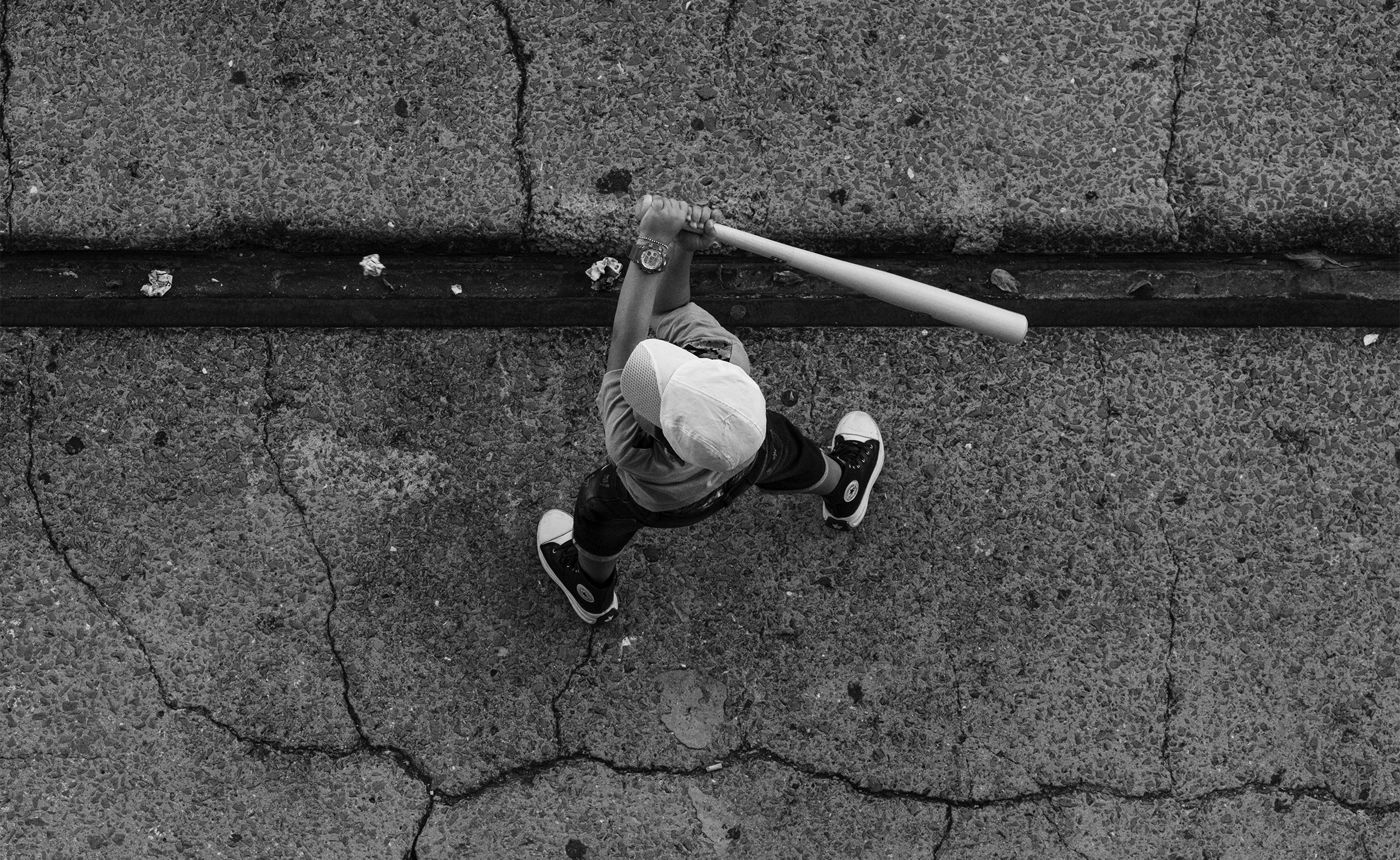 A child in a white ball cap viewed from above readies the bat as they play street baseball in Havana, Cuba.