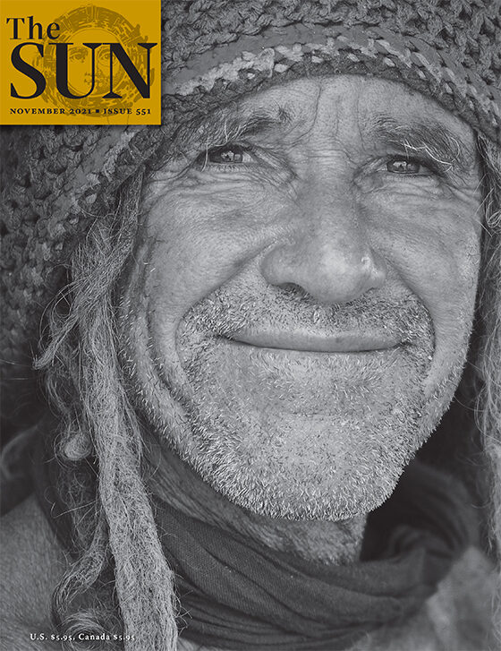 A close-up of a grizzled older man wearing a slouchie hat and a scarf. A single dreadlock escapes from the slouchie.