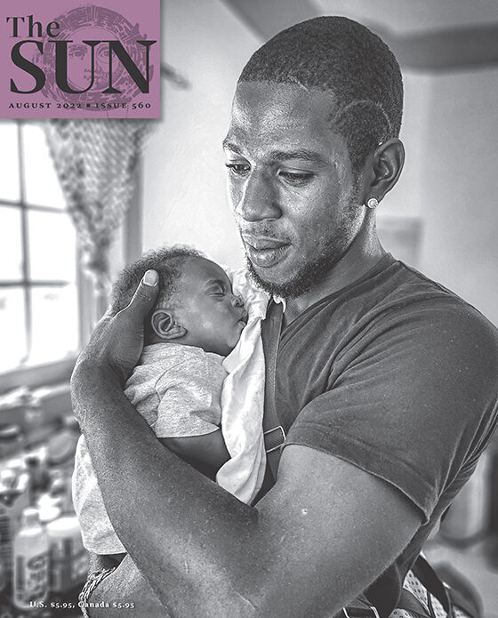 August 2022 cover of The Sun. A father holds his new son in his arms. They are in the kitchen and the infant is sleeping as the father supports his head near his shoulder.