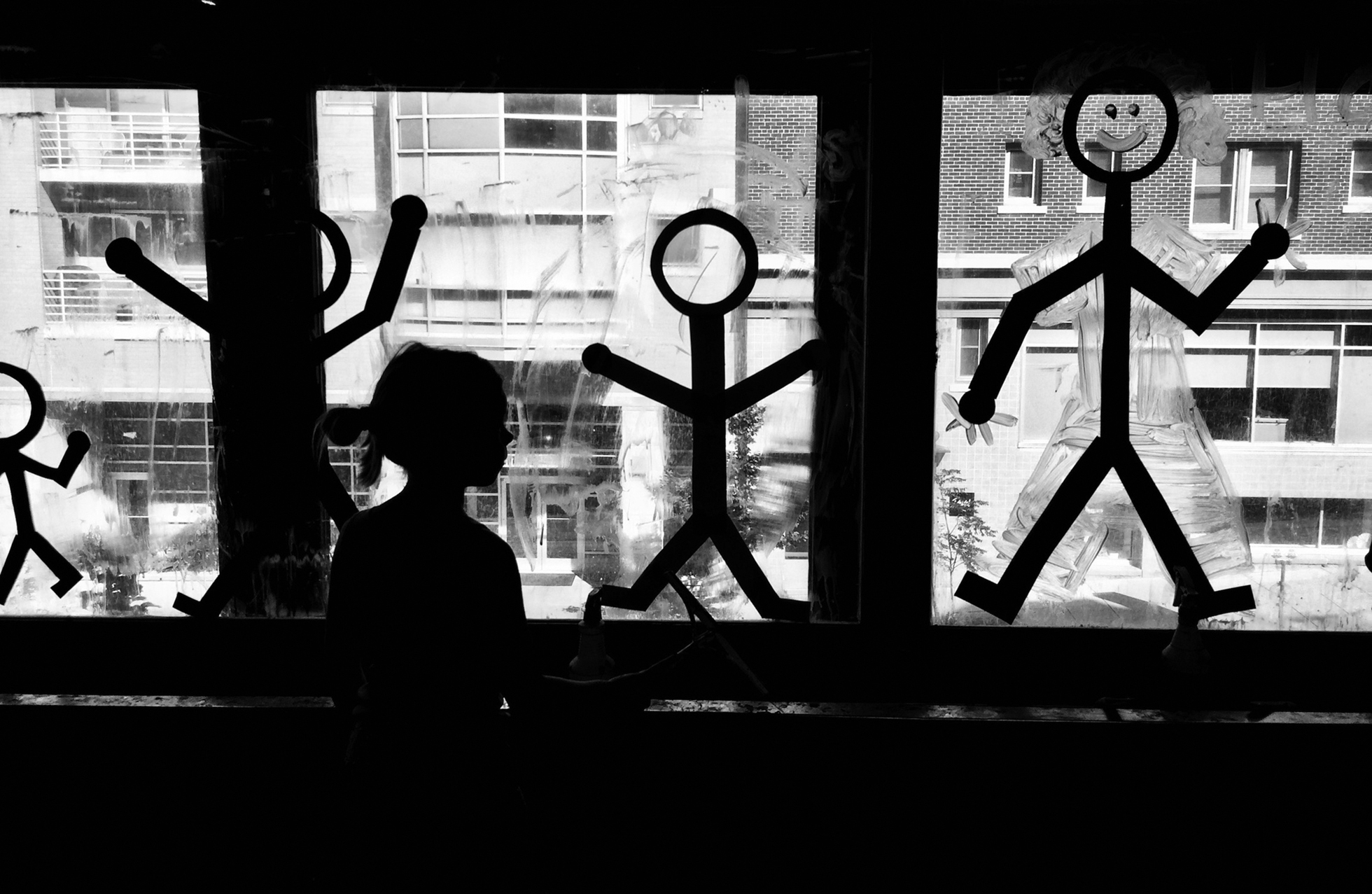 A child looks out from inside three windows of a commercial building that have stick figure decals of children and a happy adult on them.