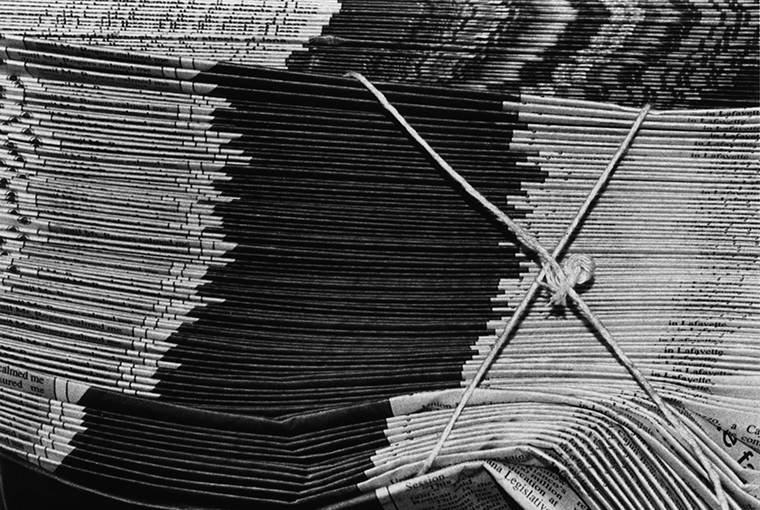 Close-up of stacks of newspapers bundled with string.