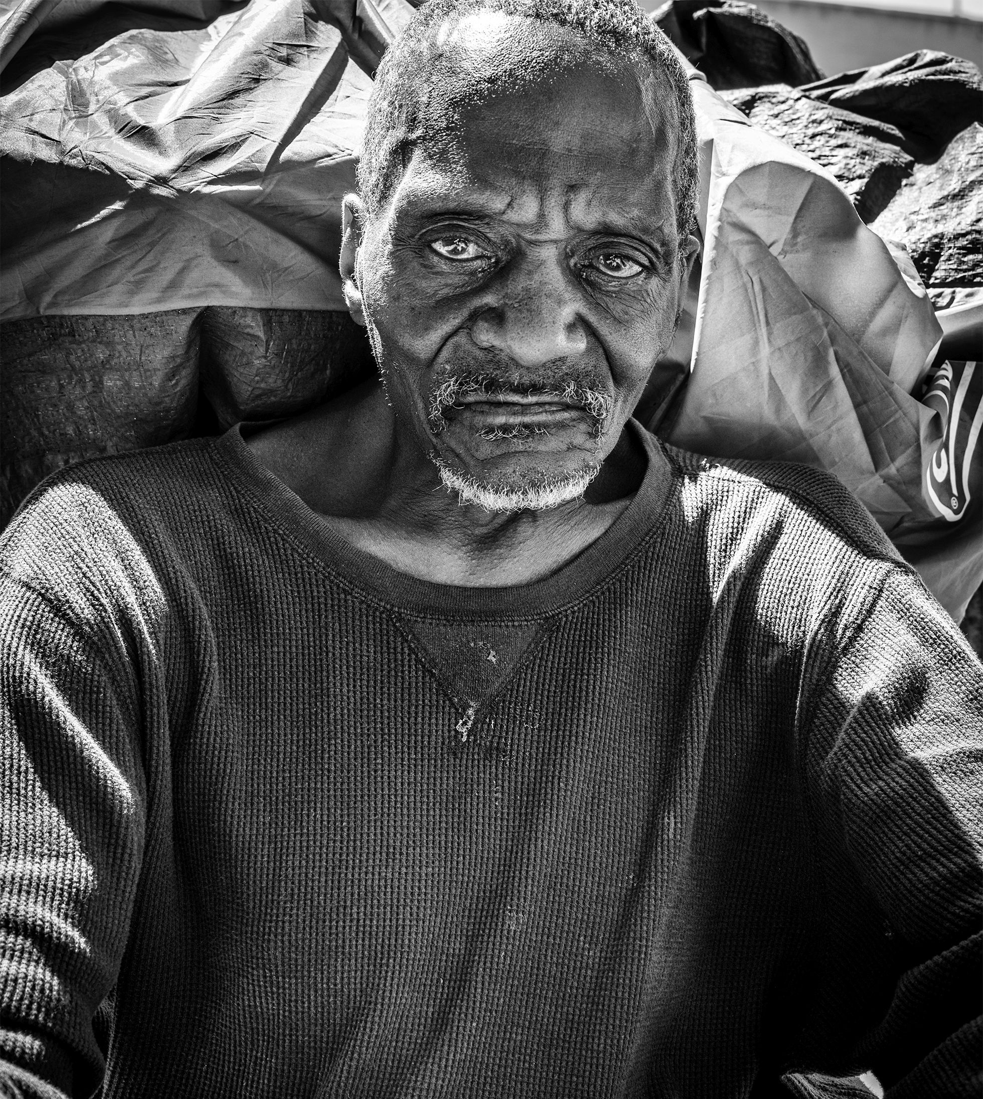 André sits in front of his tent and looks into the camera in San Francisco in August 2019. He is wearing a long-sleeved thermal crewneck shirt.