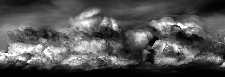 A cluster of clouds sweeps across the breadth of the image with bands of bright white interspersed with dark gray to black areas.