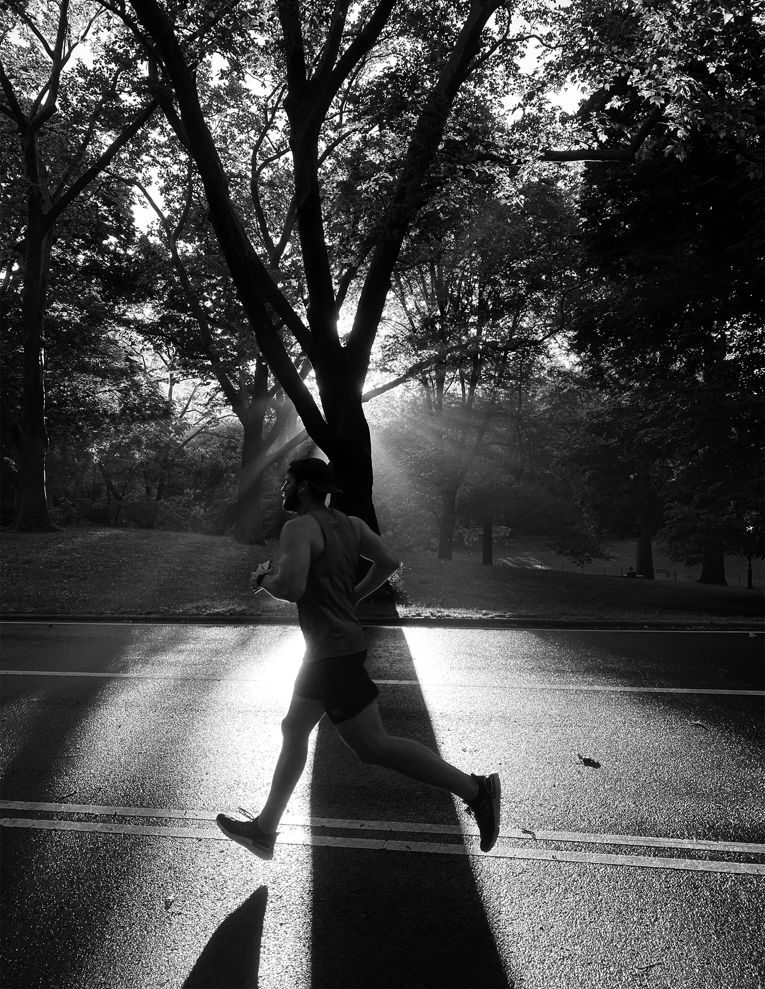 A man in a tank top and shorts runs down the centerline of a road with a parklike setting in the background.