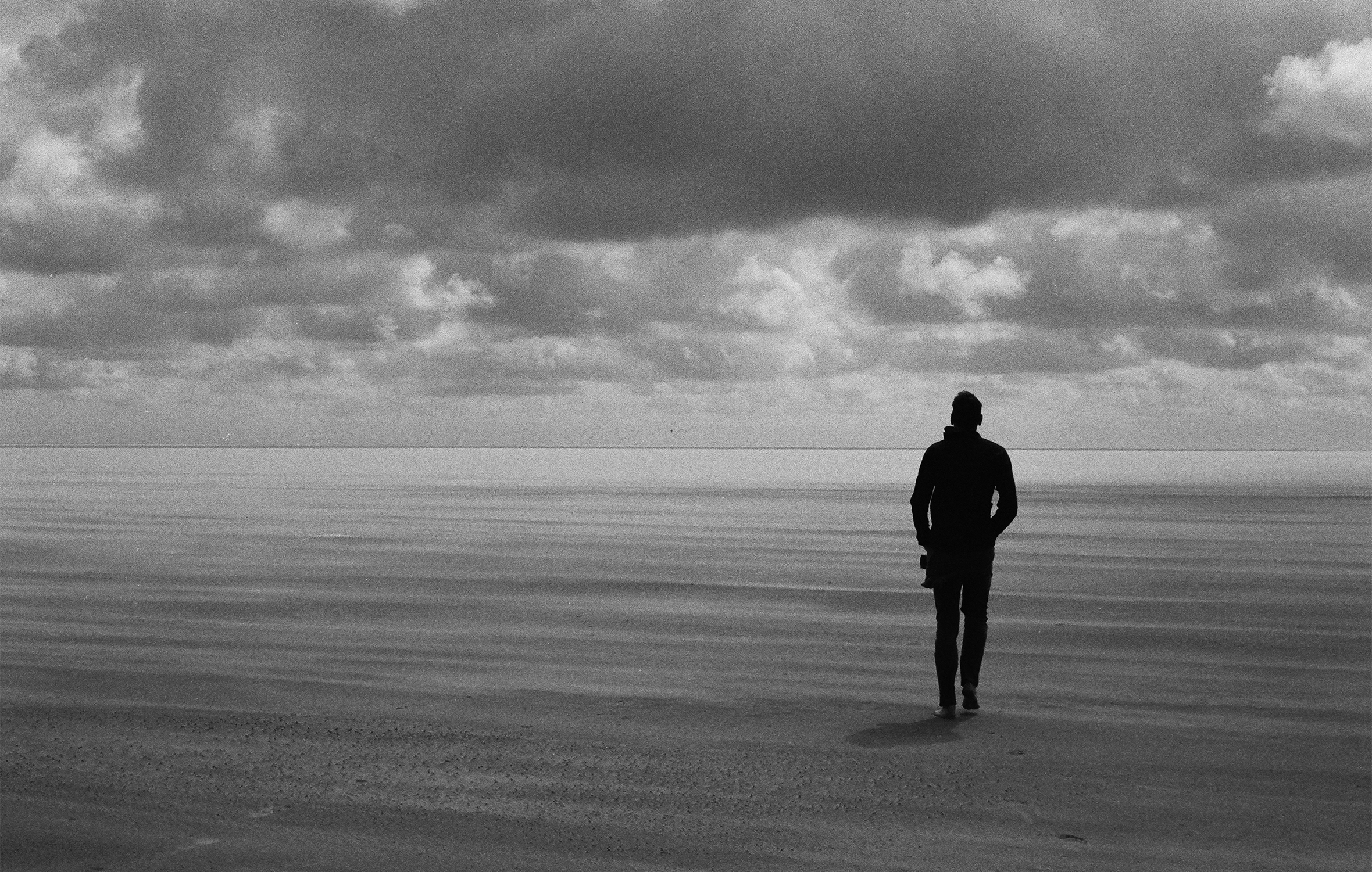 A man with his back to the camera walks on a windswept beach on a cloudy day in Sankt Peter-Ording on Germany’s North Sea coast.