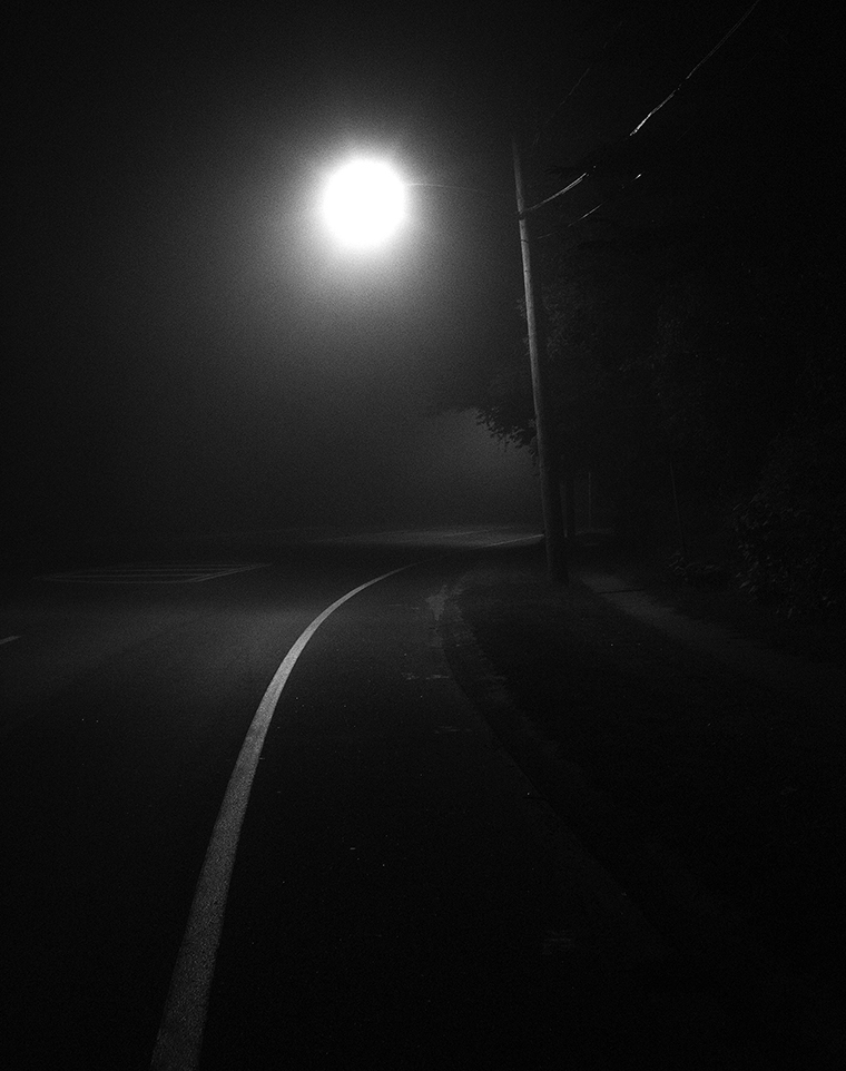 A blurry two-lane road at night that is illuminated by a streetlight.