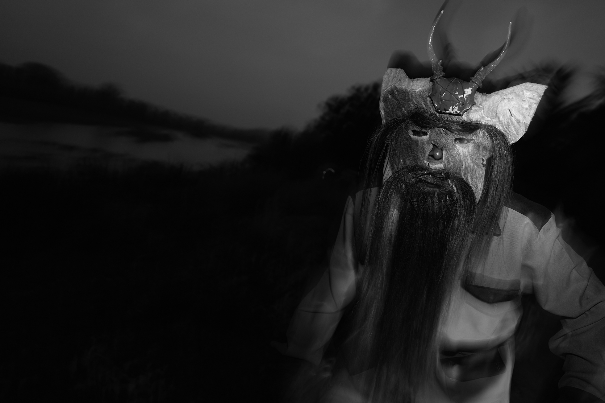 A man performs La Danza de los Diablos wearing a mask with horns and long hair, mustache, and beard.