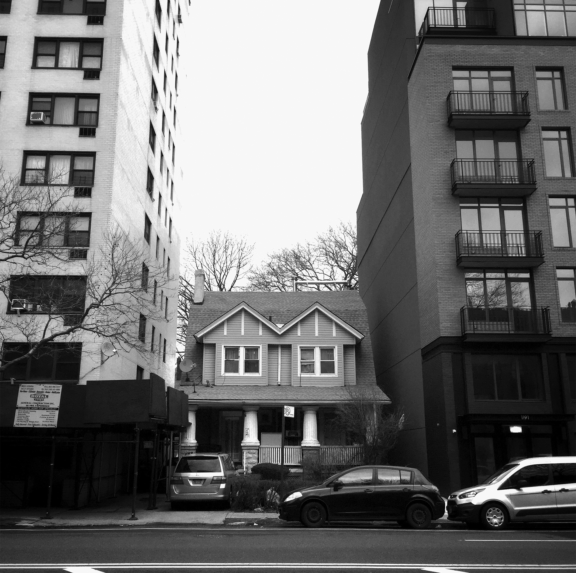 A small two-story house is sandwiched between two high-rise apartment buildings.